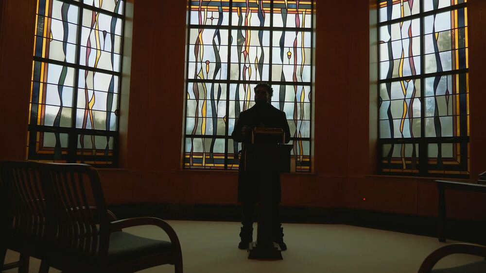Silhouette at a lectern in front of stained glass